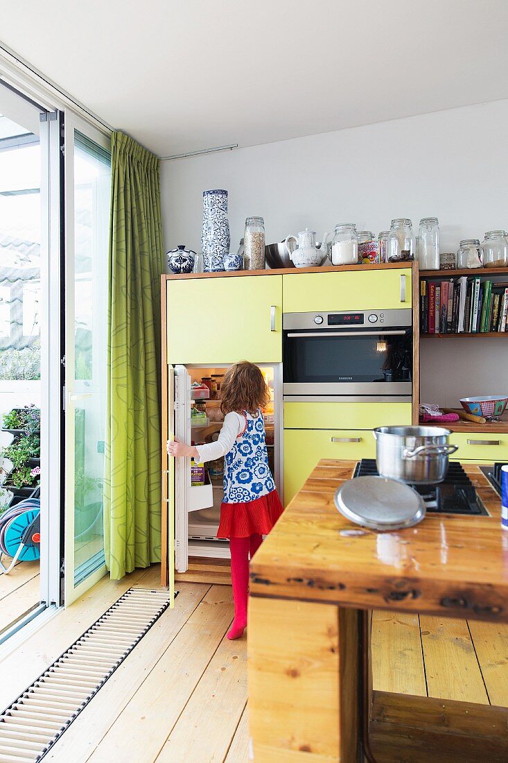 Yellow kitchen cabinets next to sliding terrace doors with child in front of open fridge