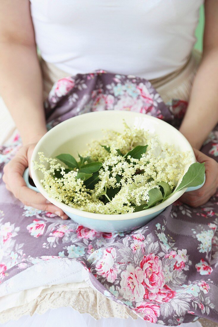 Woman's hands holding bowl of elderflowers on floral fabric