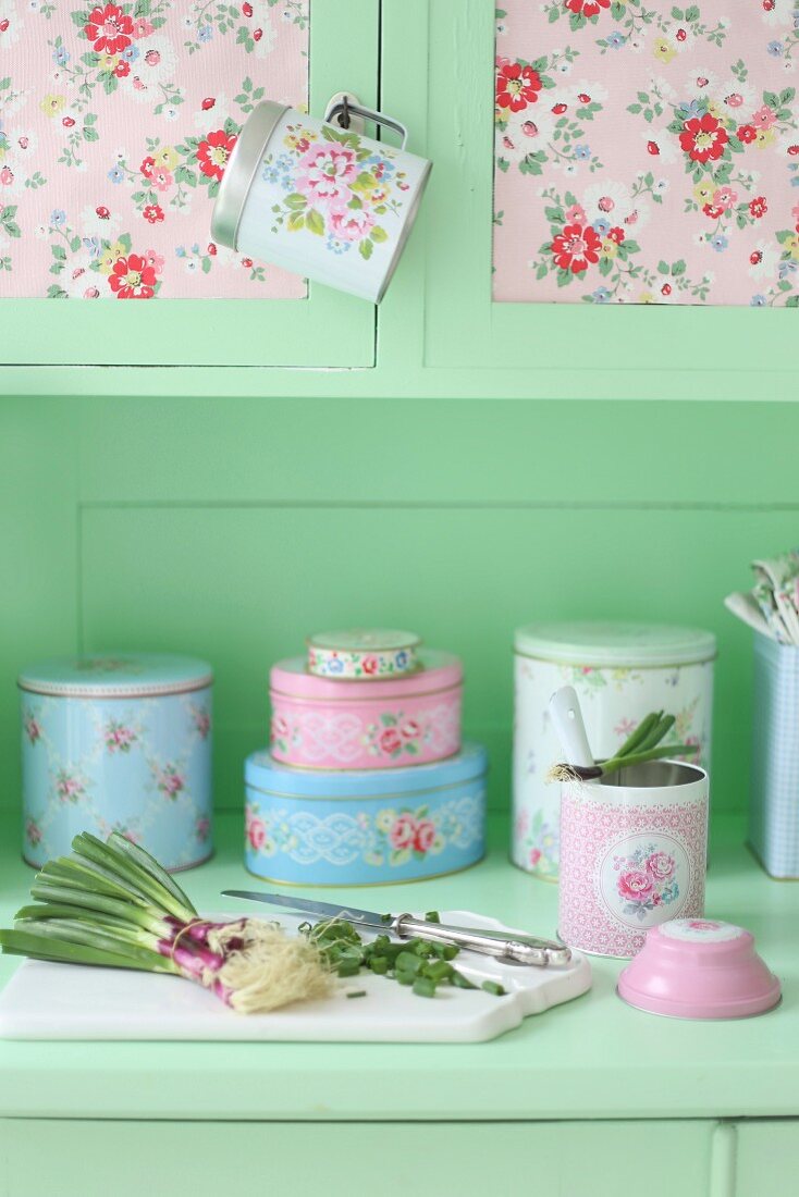 Vintage kitchen dresser with collection of romantic tins and spring onions on chopping board