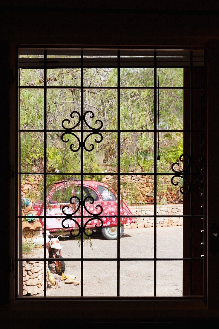 Blick aus einem Fenster mit Metallgitter auf ein bunt bemaltes Auto