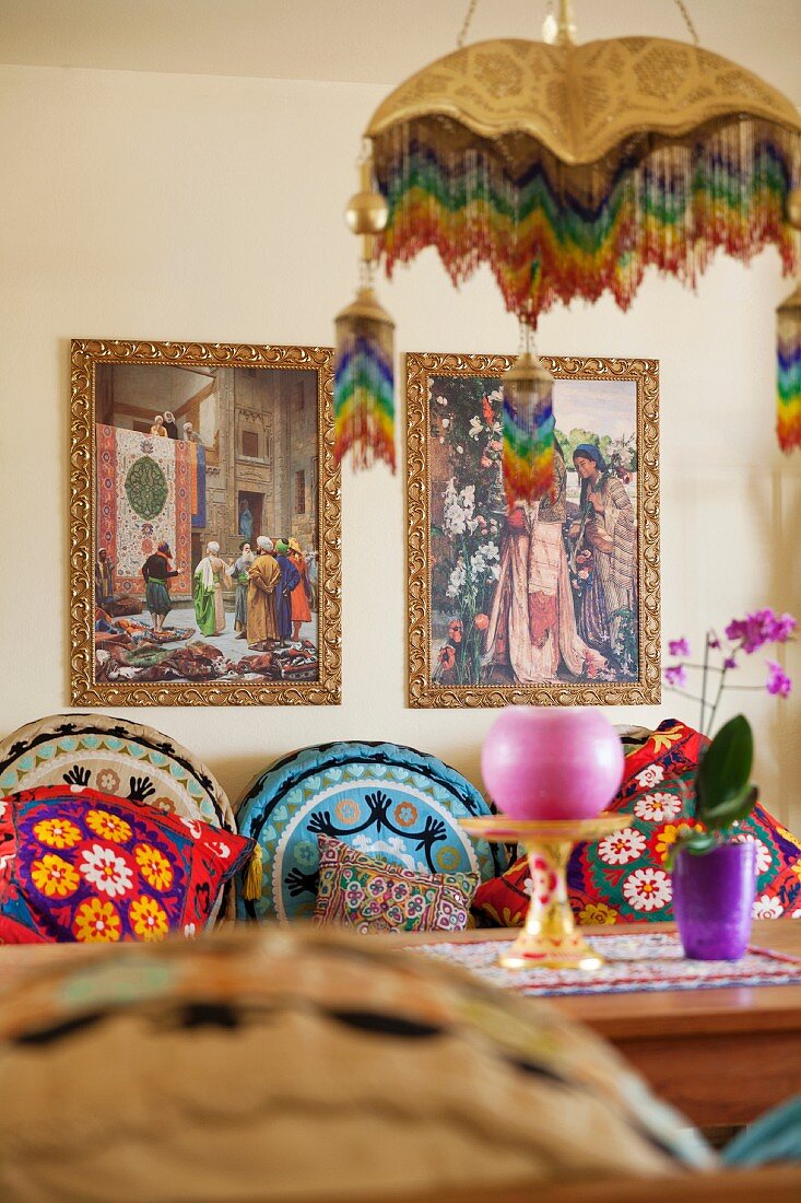 Various brightly patterned scatter cushions on bench, dining table and two Oriental pictures on wall