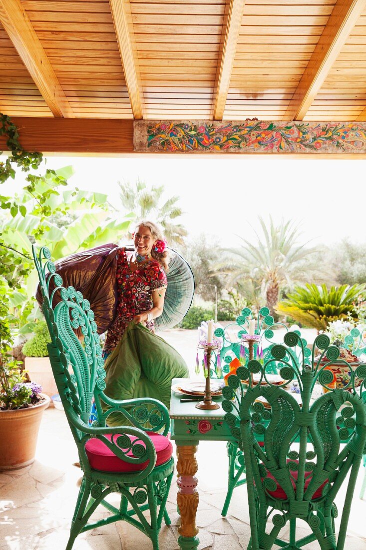 Eine fröhliche Hippie-Frau auf einer mediterranen Terrasse mit türkisfarbenen Pfauensesseln