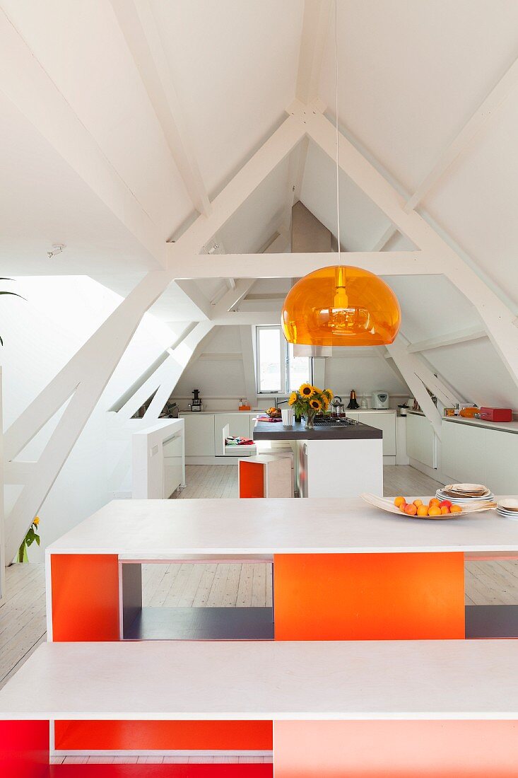 Designer table and bench set with brightly-painted inner sides below pendant lamp in open-plan kitchen