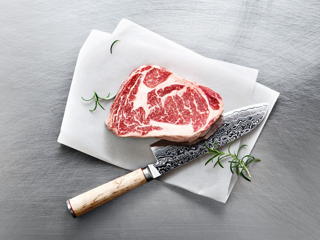 Wagyu Ribeye Steak mit Rosmarin und Messer auf Pergamentpapier