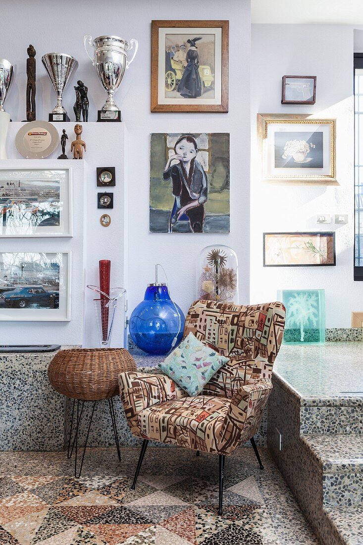 Patterned, retro armchair on mosaic floor below gallery of pictures on wall