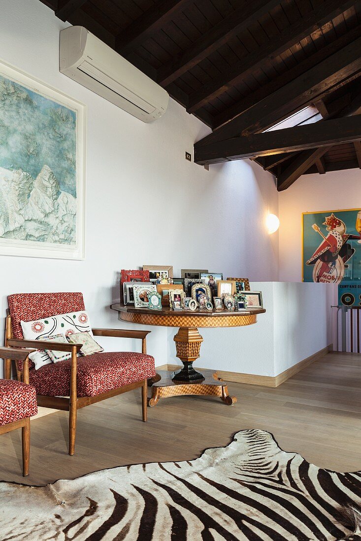 Retro armchair next to round antique table and zebra-skin rug in converted attic