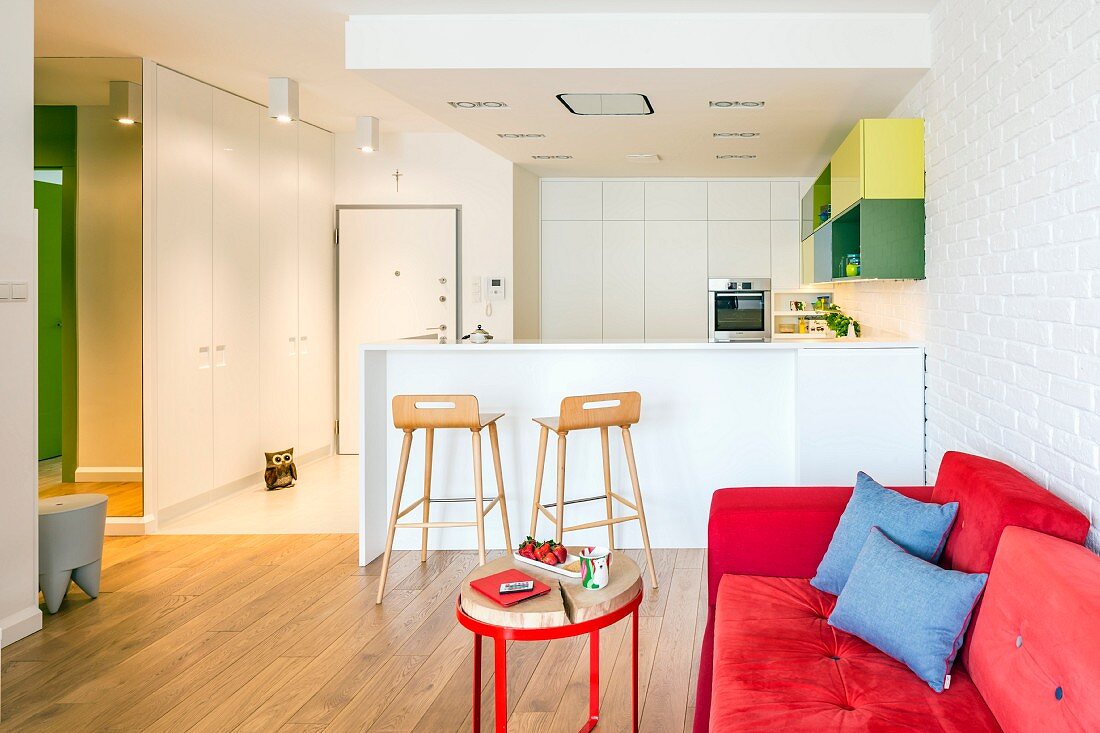 Red sofa and white fitted kitchen with breakfast bar in open-plan living area