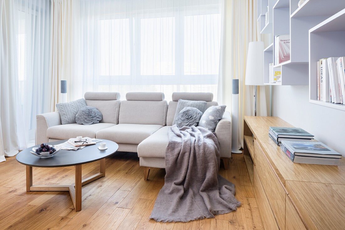 Pale couch and coffee table in front of window next to pale wood, fitted sideboard