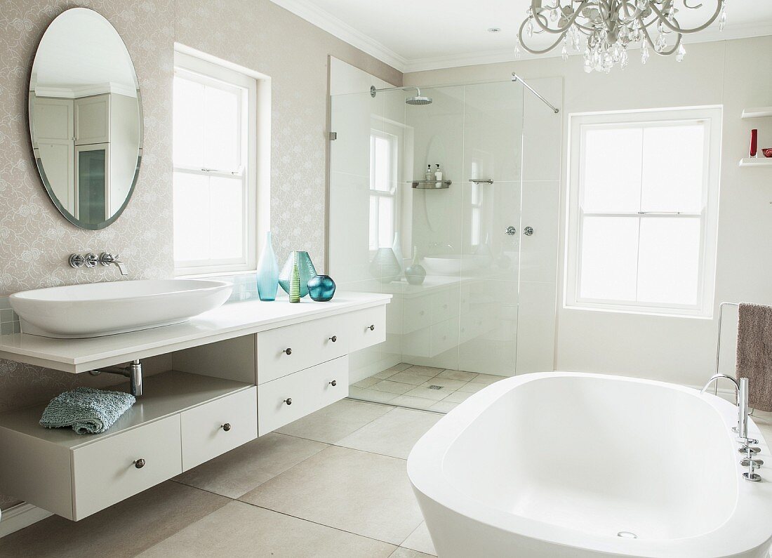 Elegantes Bad mit freistehender Badewanne, Waschtischzeile und ovaler Wandspiegel, verglaste Dusche in der Ecke