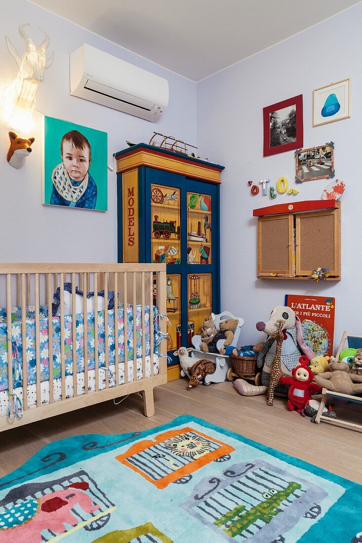 Fröhlich buntes Kinderzimmer, Teppich mit Tiermotiven, Gitterbett, bemalter Kleiderschrank un Stofftiere