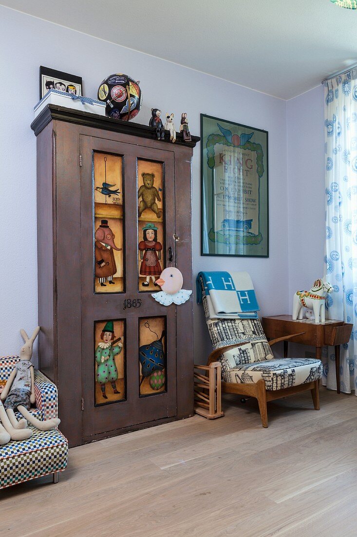 Cupboard with painted door panels next to retro armchair against wall painted pastel lilac