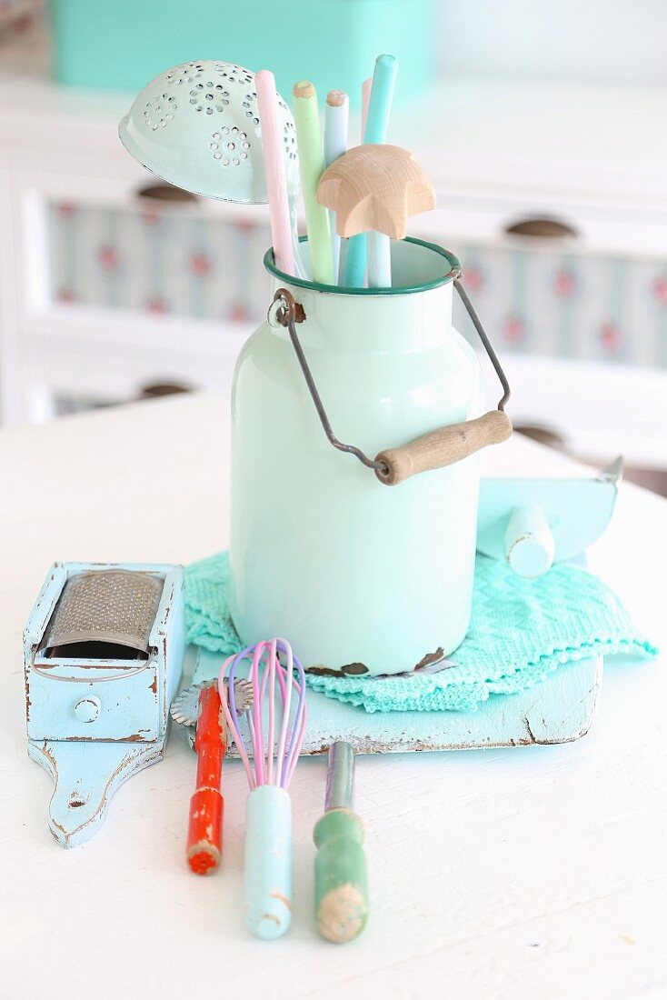 Nostalgic still-life arrangement of pastel kitchen utensils in vintage milk can