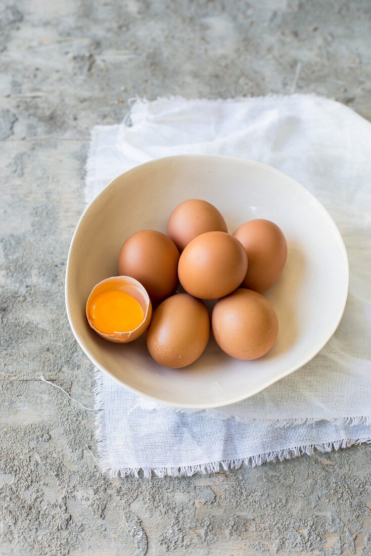 Large brown organic eggs, one cracked open, in a bowl