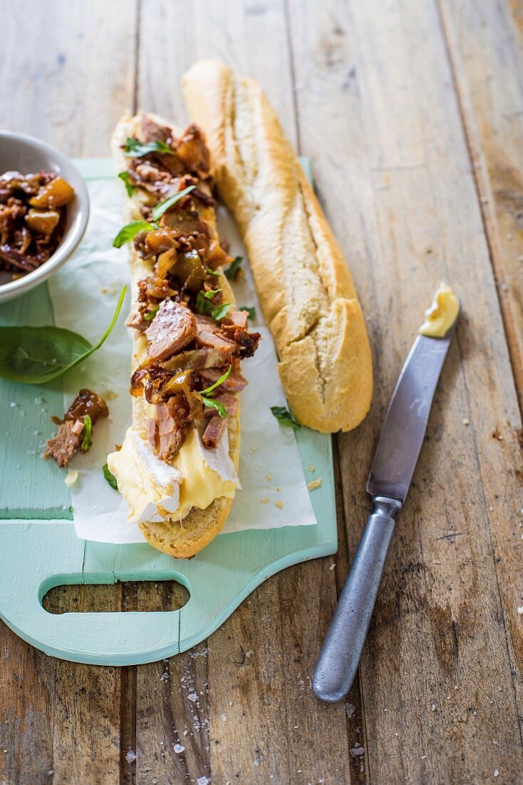 A baguette sandwich with roast pork fillets, Camembert, mustard, basil and caramelised onions