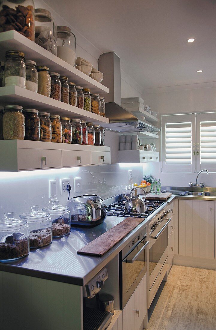 White, fitted kitchen; storage jars on shelves with drawers above kitchen counter