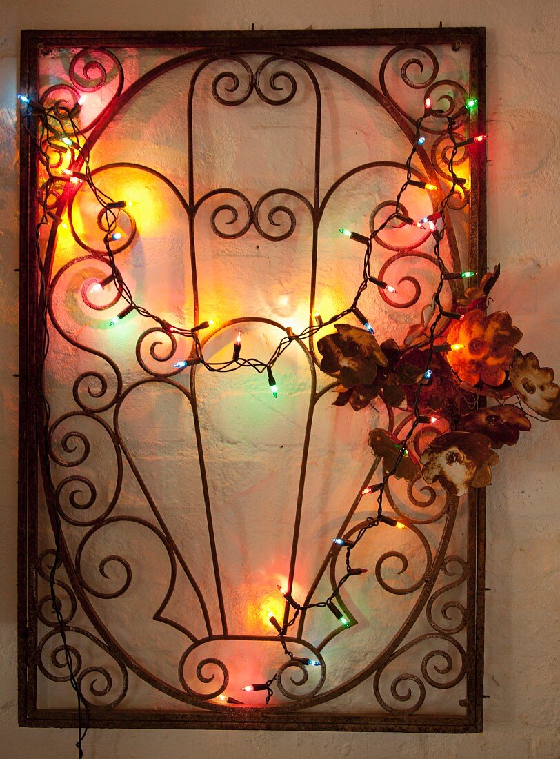 Wrought iron lattice decorated with flowers and fairy lights hung on wall