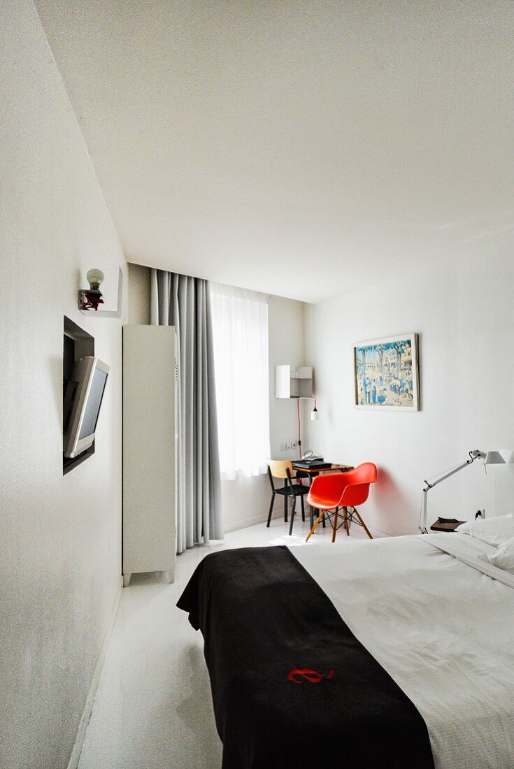 Modern hotel room with double bed, flatscreen TV recessed in wall and red, classic chair next to table in background