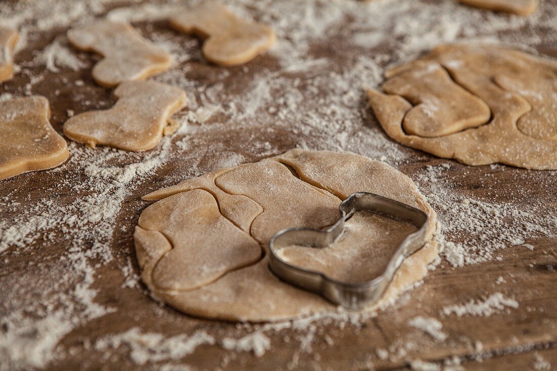 Boot-shaped shortbread biscuits being cut out on a floured work surface