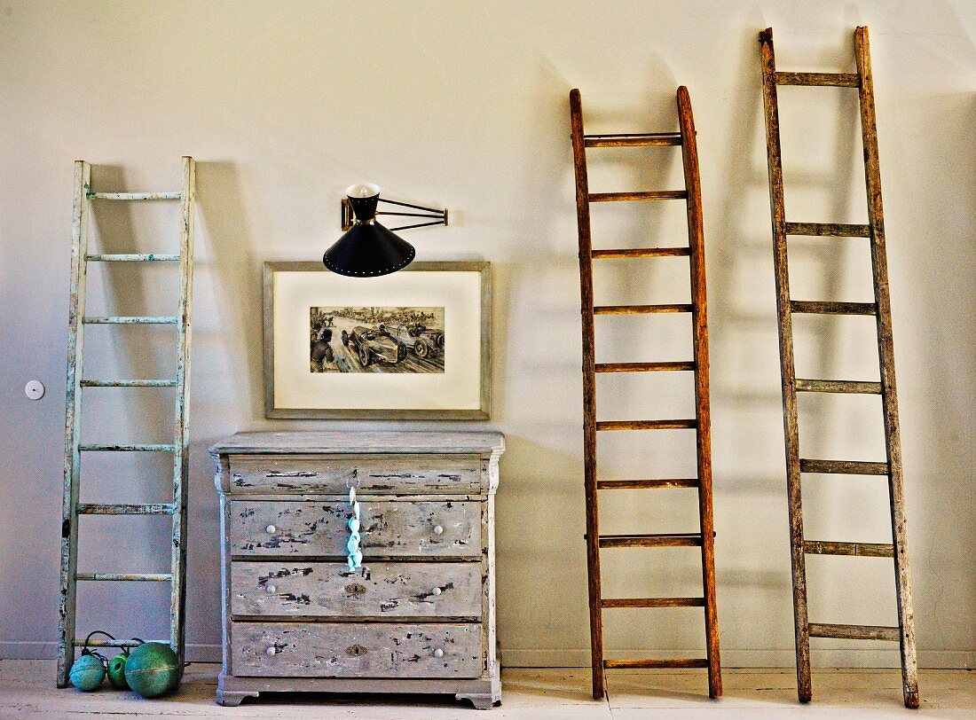 Wooden ladders leaning against wall, old chest of drawers, picture and wall-mounted lamp