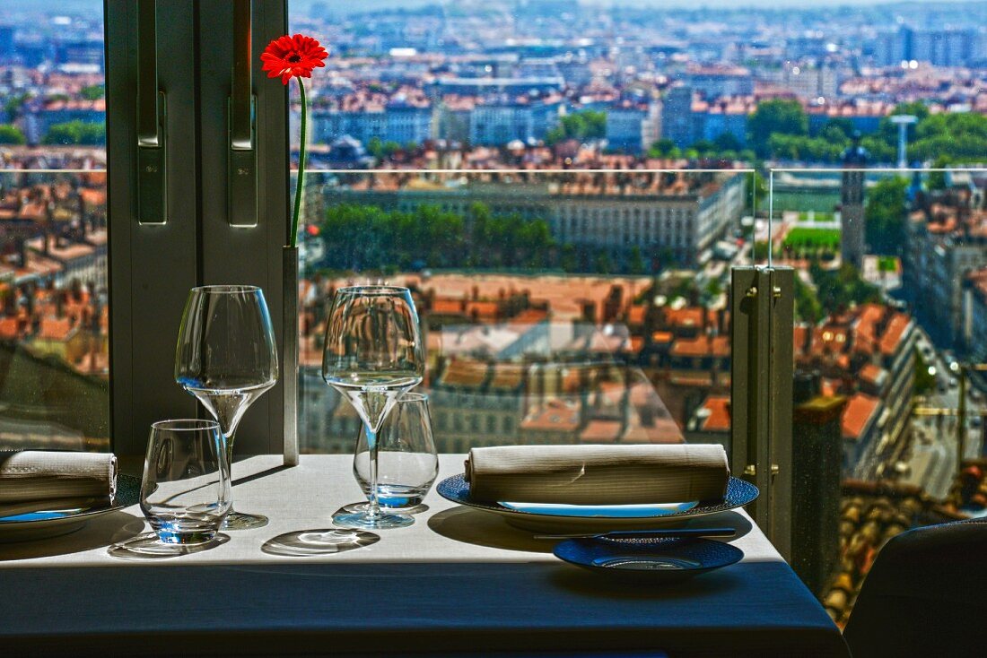 Gedeckter Tisch am Fenster mit Glasbrüstung und Blick auf die Stadt