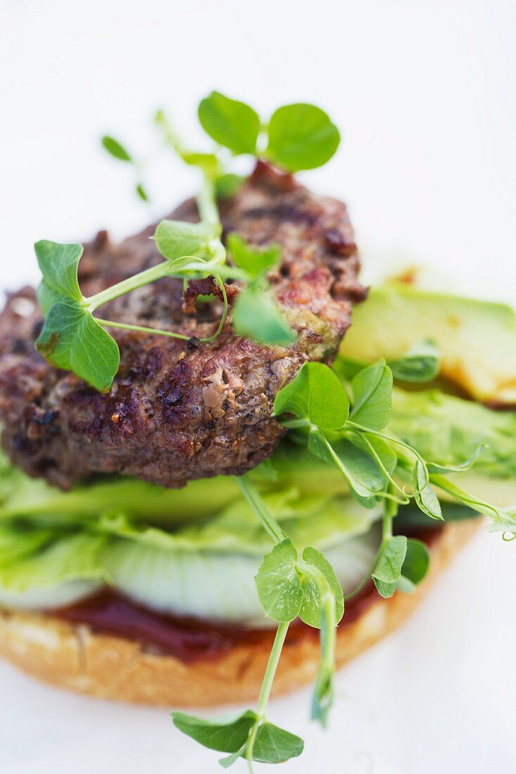 A burger with pea shoots, avocado, lettuce, onions and ketchup