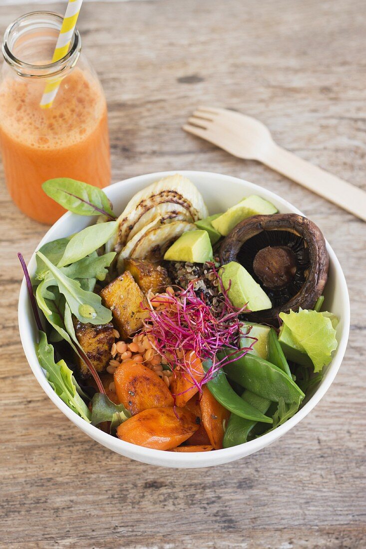 Quinoa salad with fried tofu, vegetables and mushrooms with a bottle of carrot juice