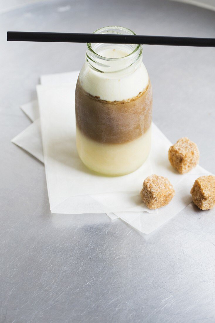 Frozen iced coffee with three layers (vanilla cream, espresso, milk) in a small milk bottle with brown sugar cubes