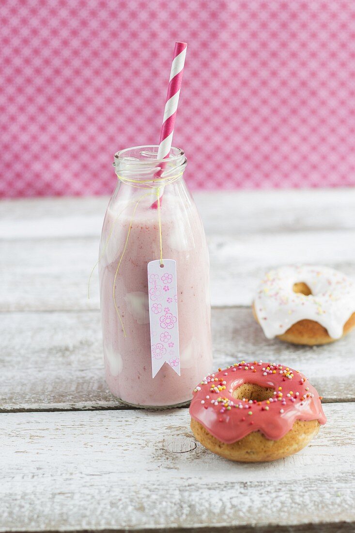 A bottle of strawberry milk with yoghurt spots and mini iced doughnuts