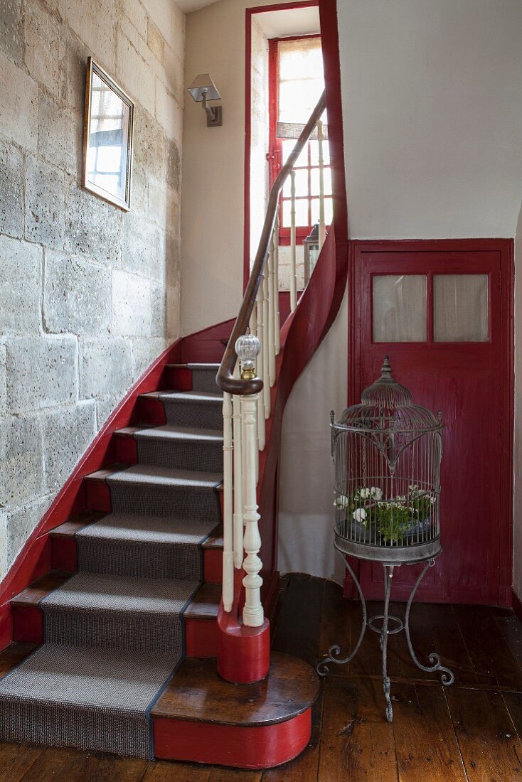 Treppenhaus eines französischen Landhauses aus dem 18. Jahrhundert in Rot und Grau mit einer Steinwand und nostalgischer Vogelvoliere