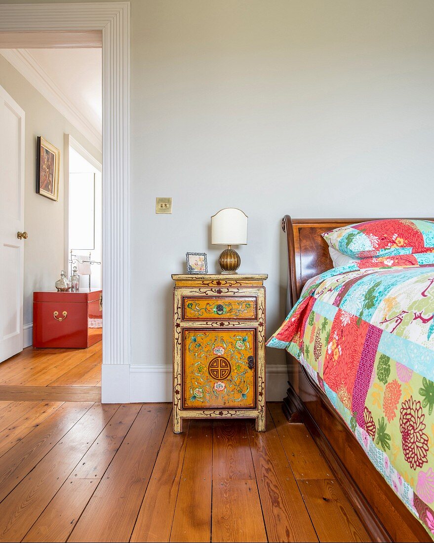 Oriental cabinet next to antique bed with patchwork quilt next to open door with view of red-painted trunk