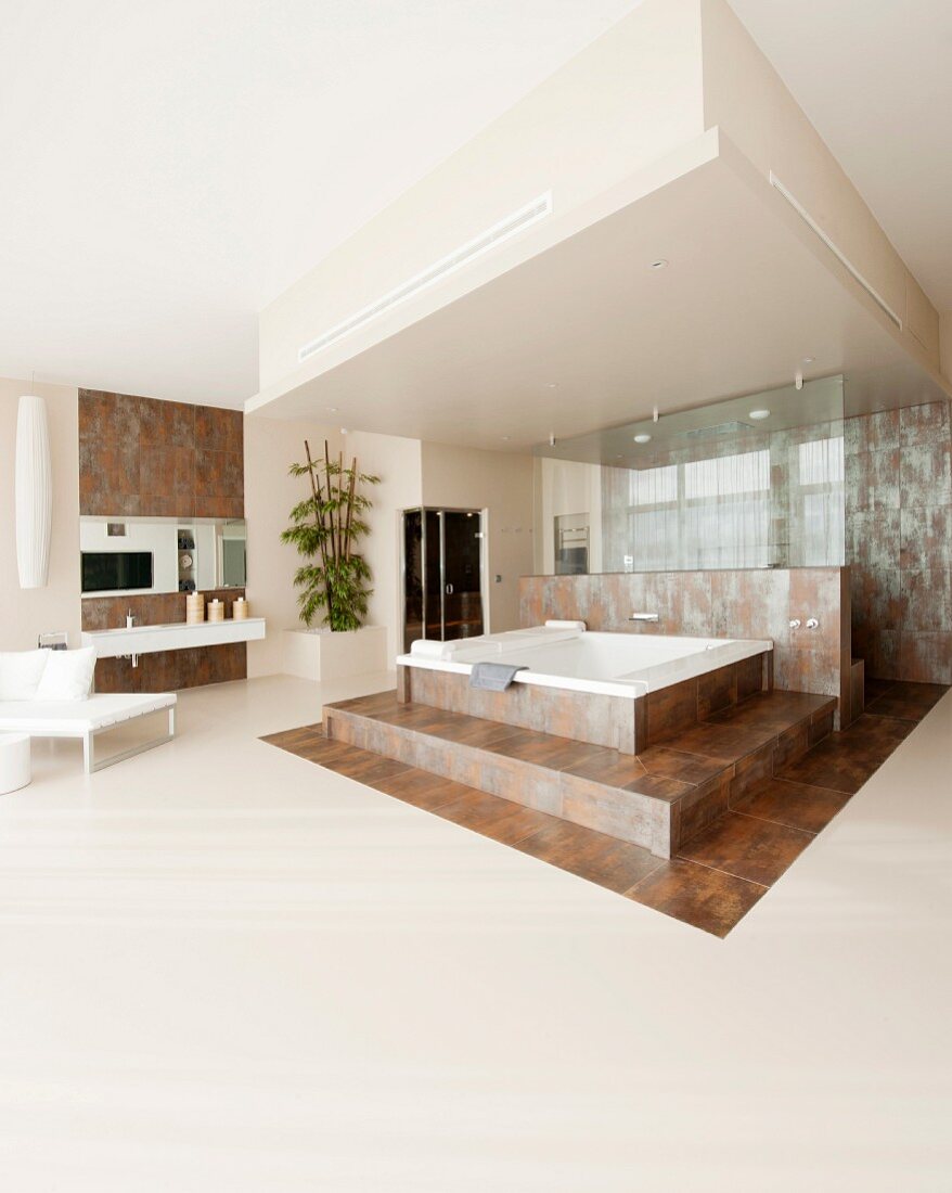 Large bathroom with whirlpool bath on platform covered in rust-effect tiles