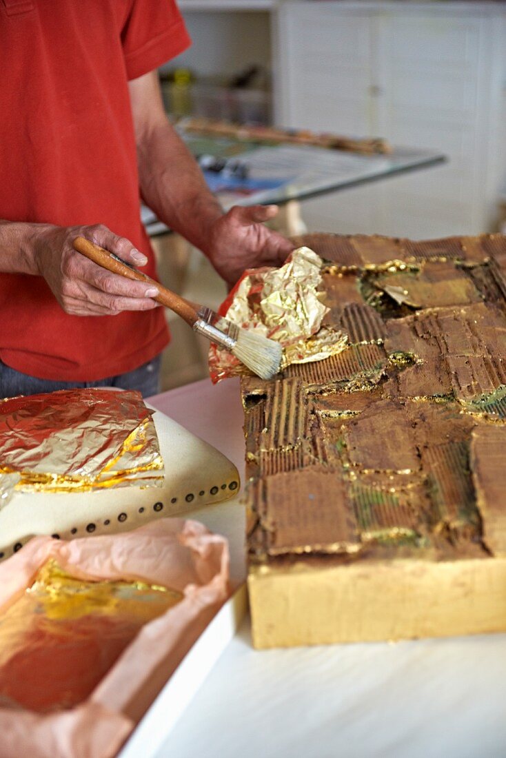 Hands of person applying gold leaf to artwork in artist's workshop