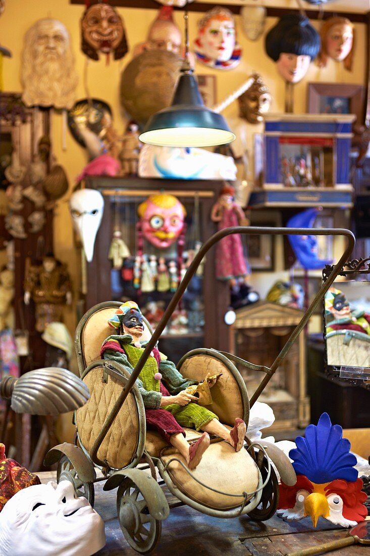 Figurine in vintage doll's pram in mask sculptor's workshop