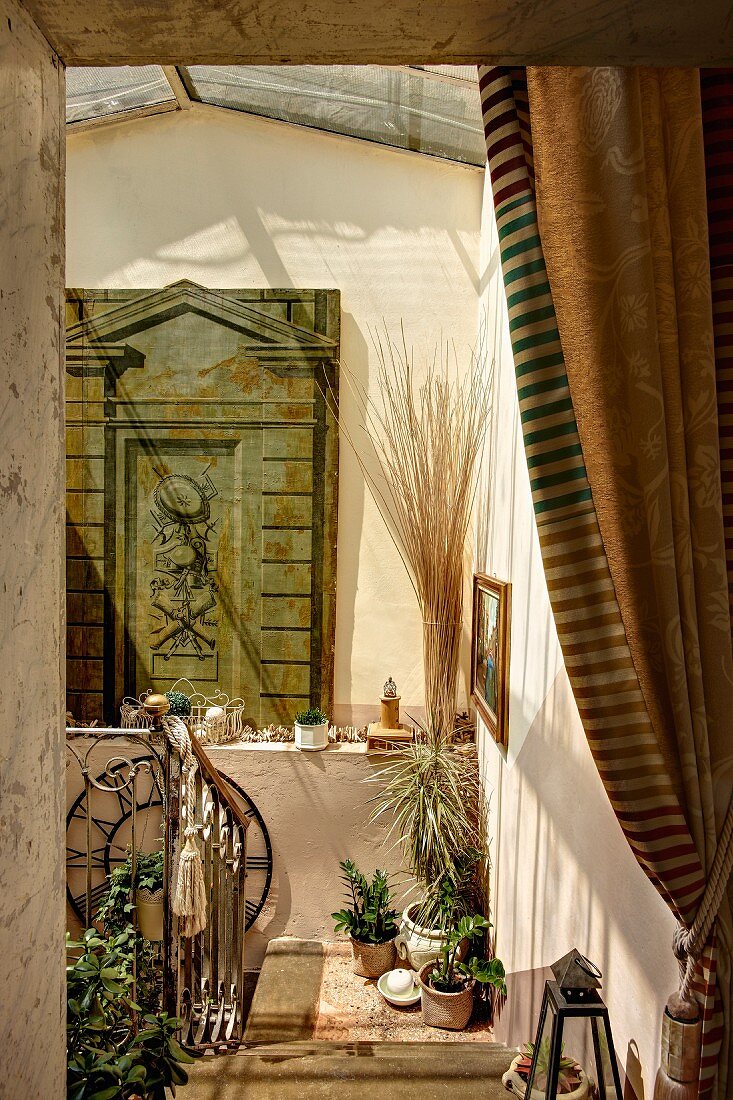 View into sunny stairwell with potted plants on floor and painted wooden panel on shelf