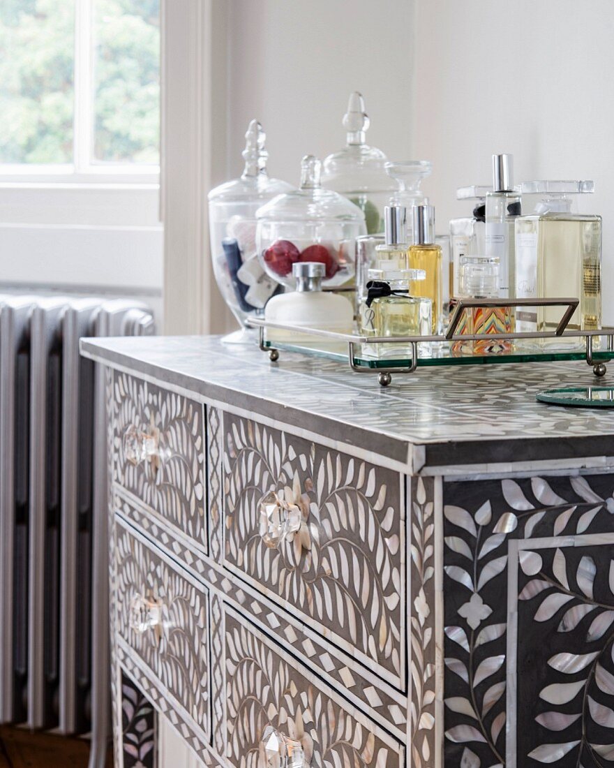 Various perfume bottles on tray on top of chest of drawers inlaid with mother-of-pearl