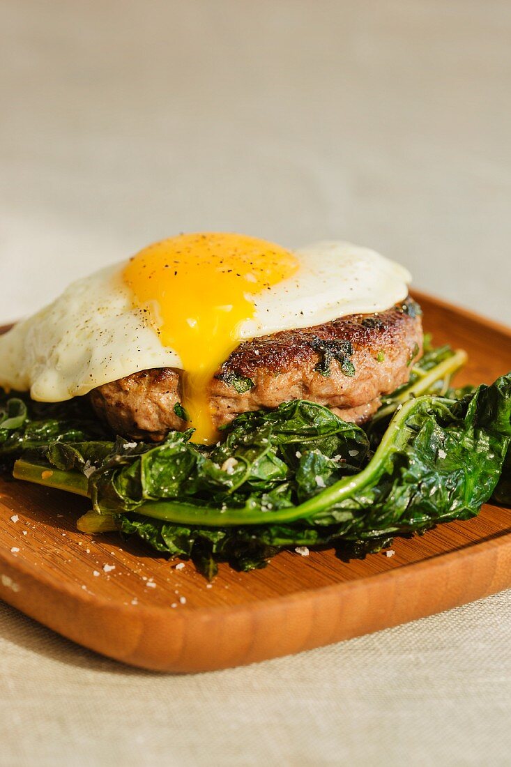 A grilled lamb burger topped with a fried egg and served with sautéed kale