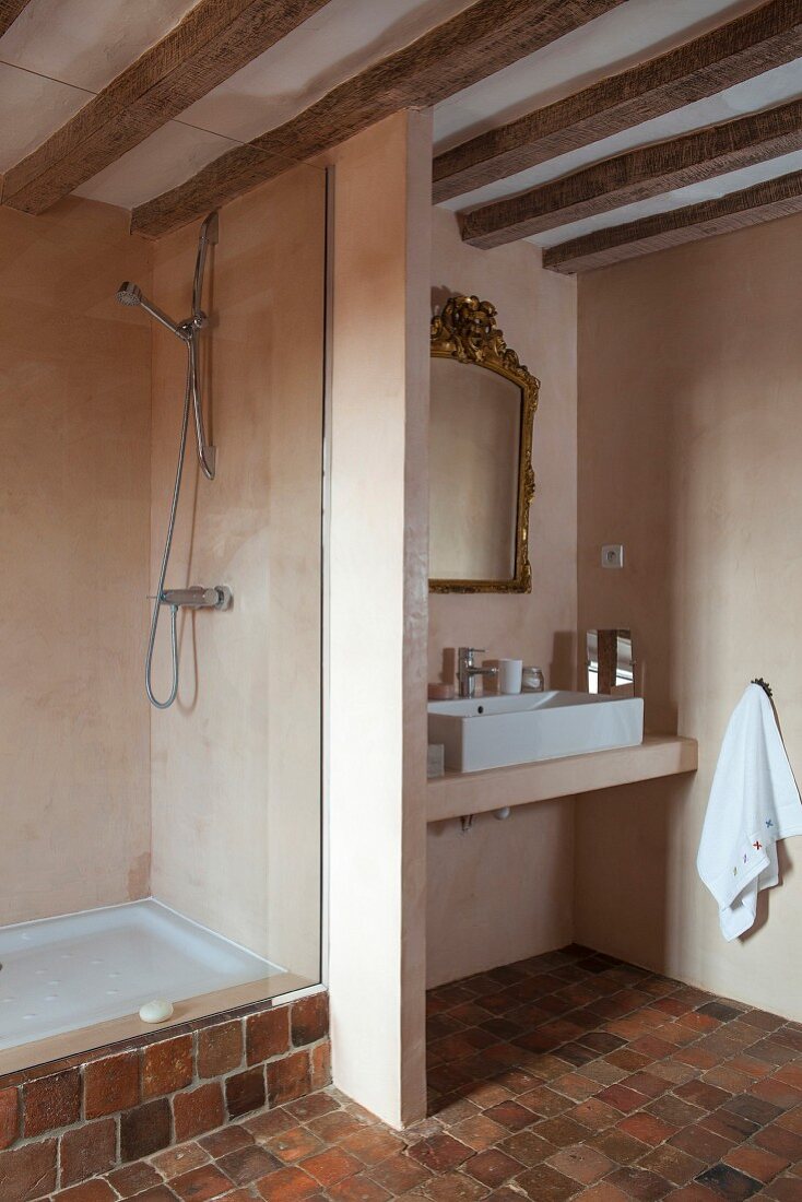 Wood-beamed ceiling, stone-tiled floor and partition between sink and shower areas in rustic bathroom