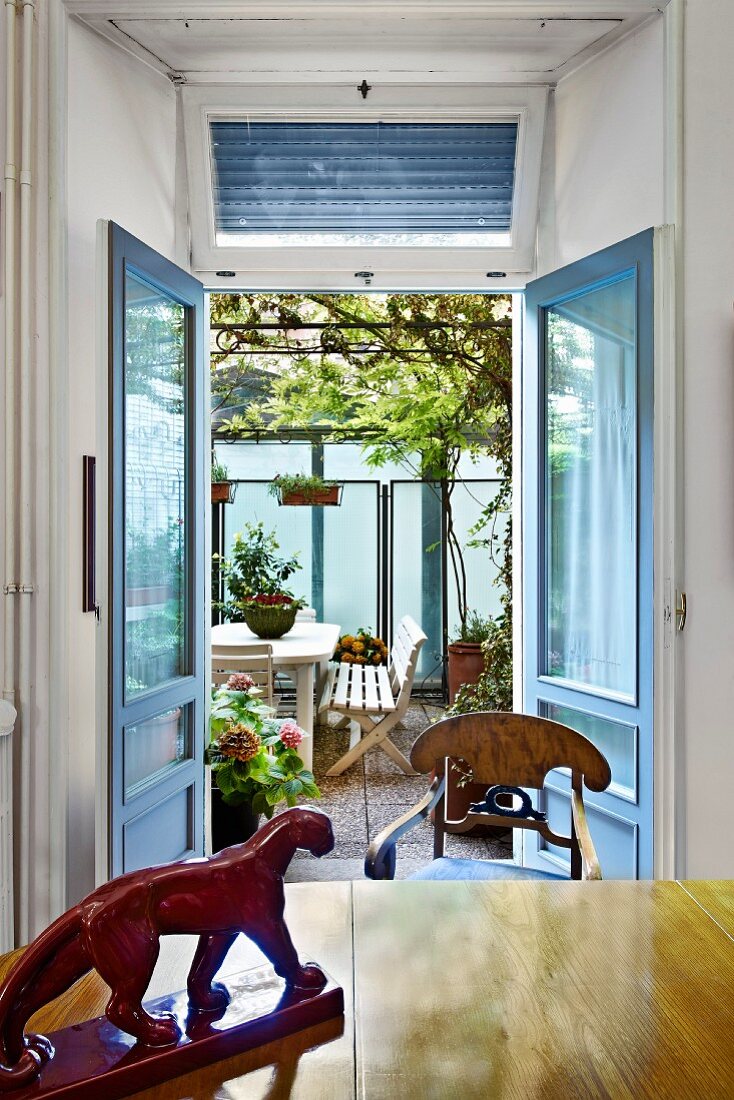 View past wooden animal figurine on table through open double doors to seating area in courtyard