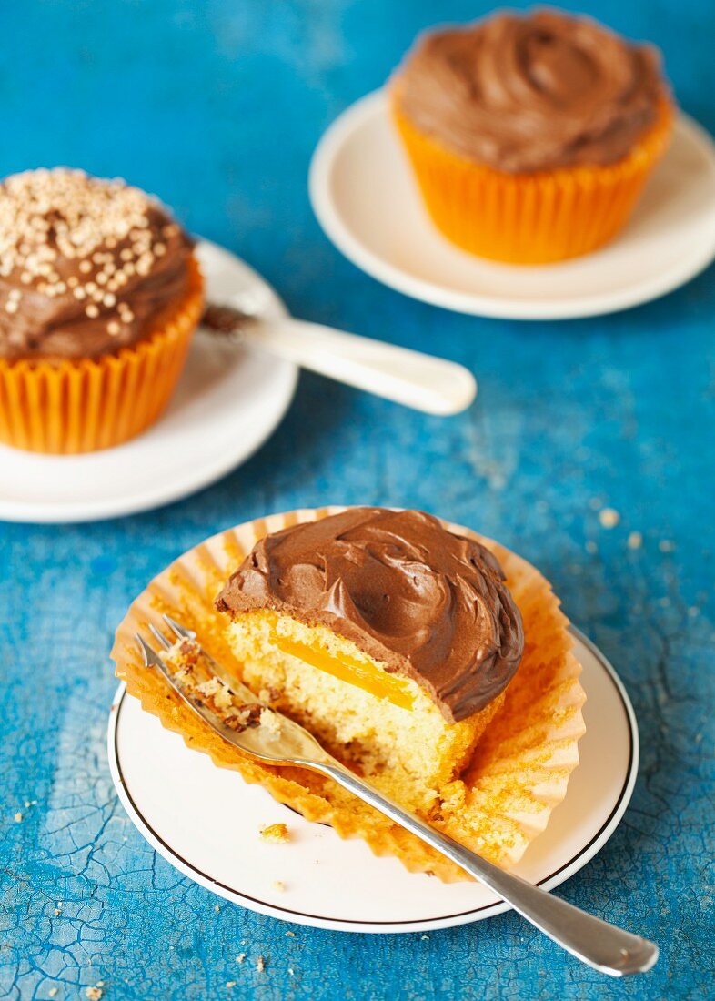 A half-eaten vanilla cupcake with orange and chocolate cream