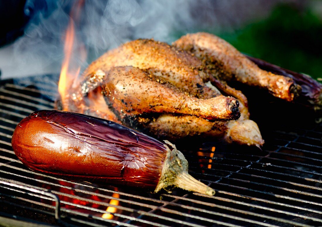 A whole chicken and an aubergine on a barbecue