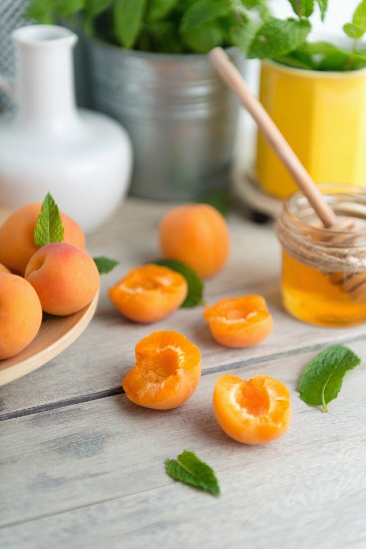 Apricots, whole and halved, on a wooden table with a jar of honey