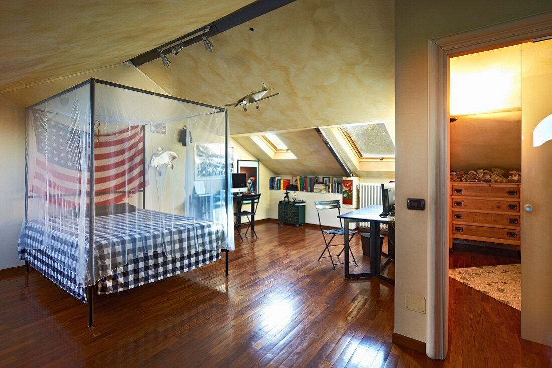 Baldachinbett mit Moskitonetz und amerikanischer Flagge in Dachraum mit Schreibplatz unter Dachflächenfenster