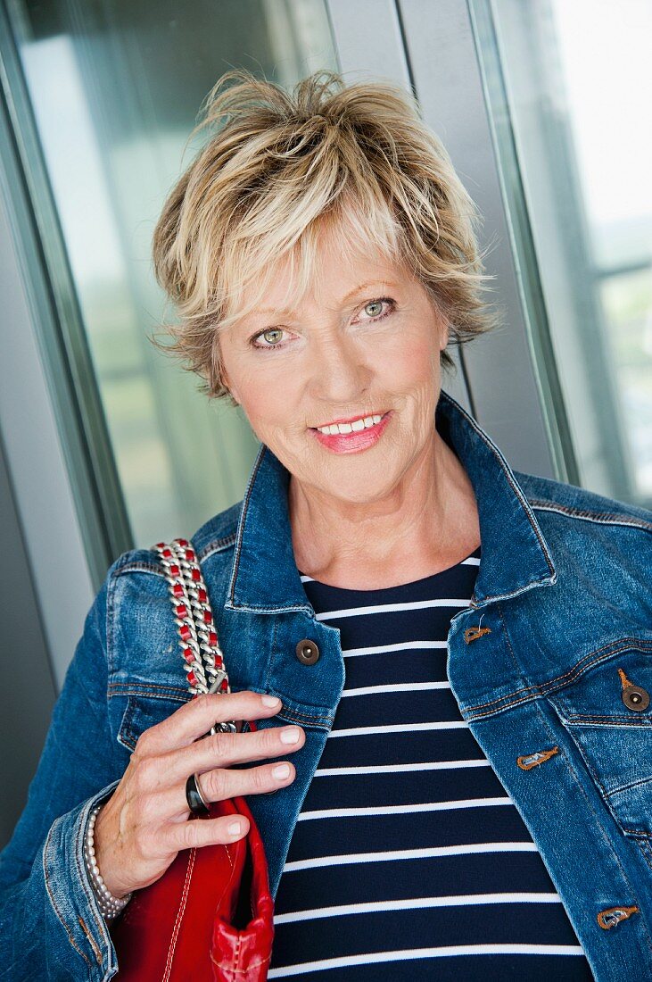 A portrait of an older woman in a denim jacket and a stripped shirt