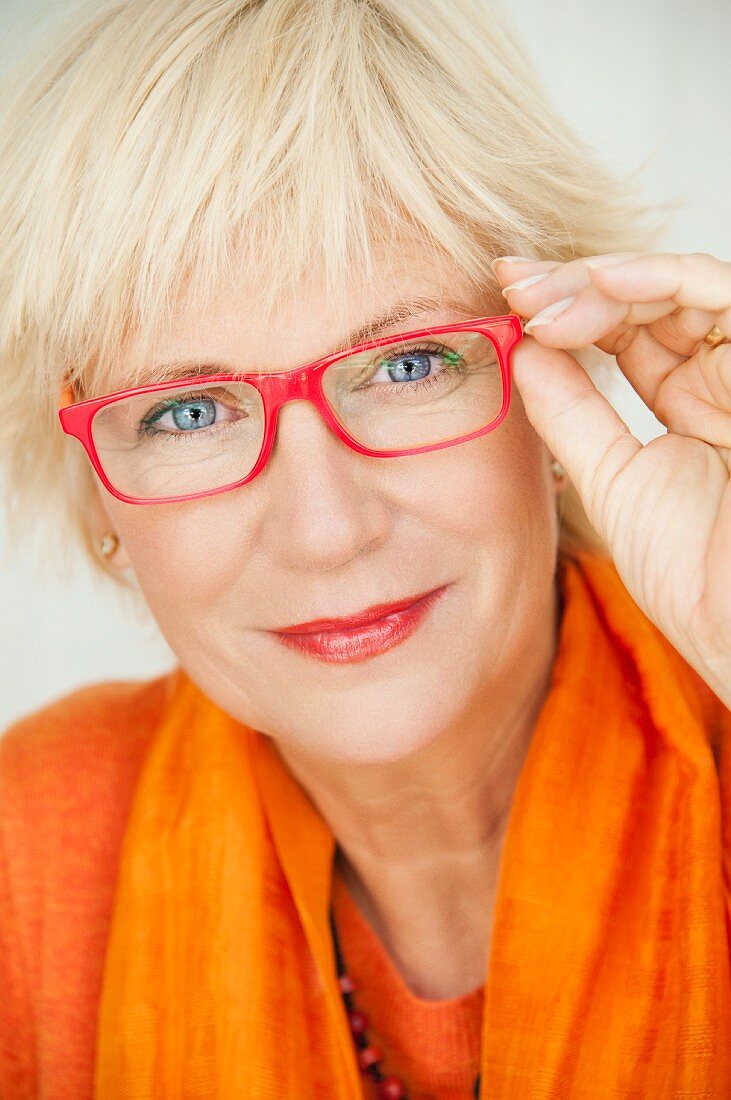 An older woman wearing an orange jumper and scarf and a pair of red glasses