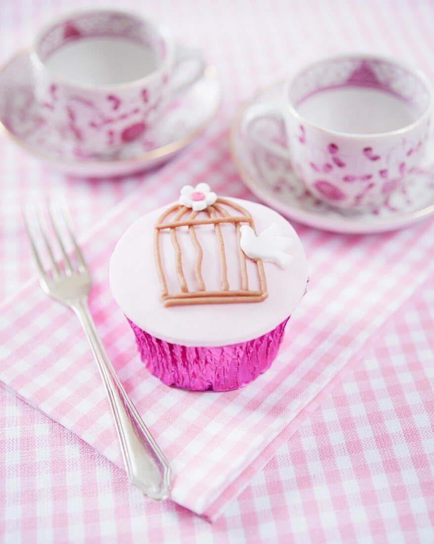 A cupcake decorated with a birdcage and a dove