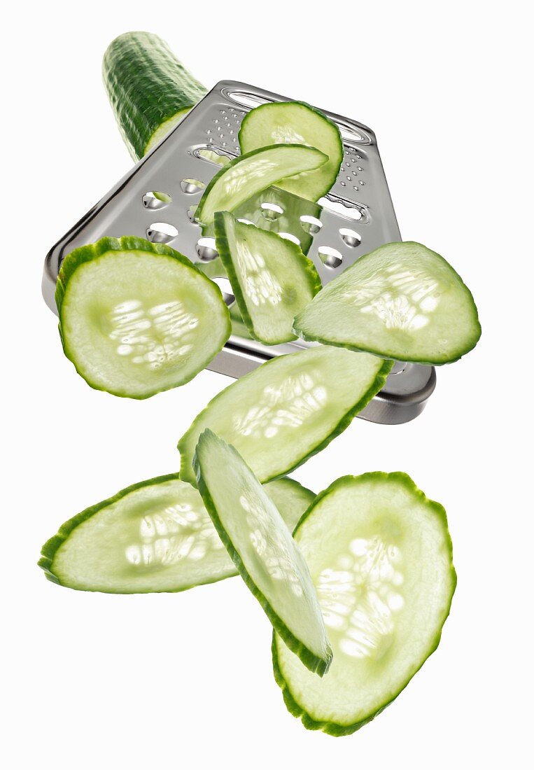 A grater with a cucumber and cucumber slices
