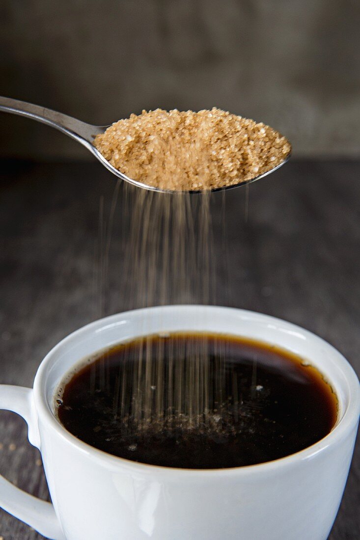 Braunen Zucker in Kaffeetasse streuen