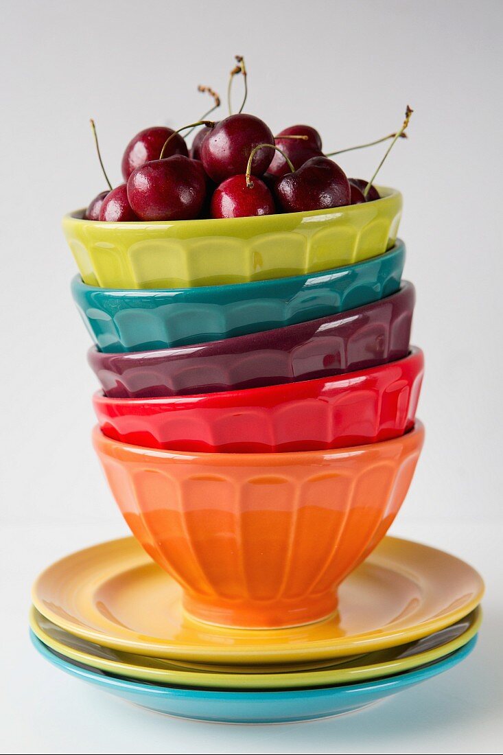 Cherries in the topmost of a stack of colourful bowls