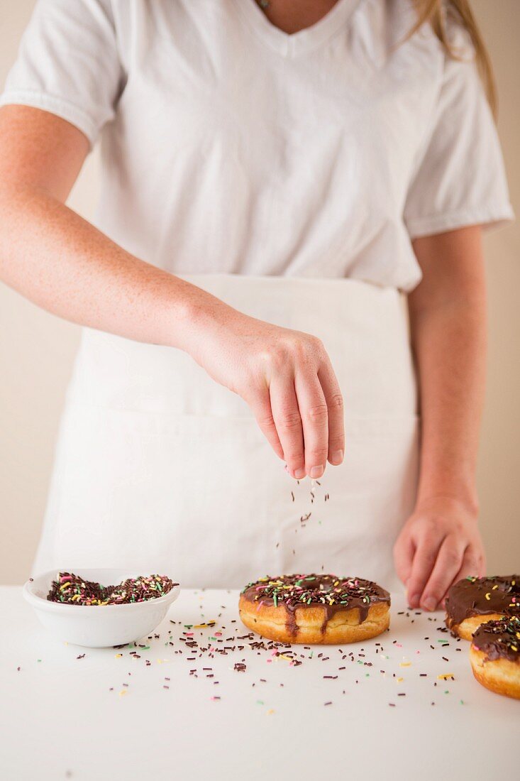 Chocolate-glazed doughnuts being sprinkled with hundreds and thousands