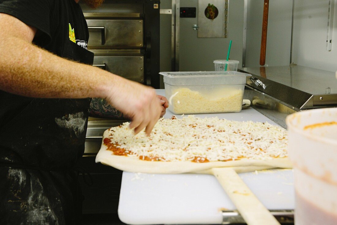 Pizzabäcker bestreut ungebackene Pizza mit Käse